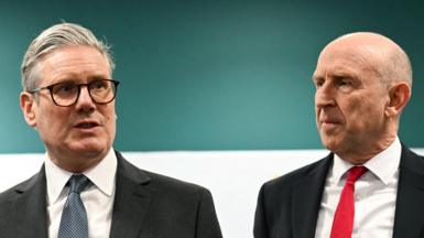 Sir Keir Starmer and John Healey pictured together. Both men are wearing dark suits and white shirts, with Sir Keir in a blue tie and Healey in a red tie.