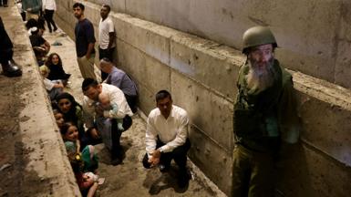 A person in military uniform looks away from camera alongside a group of people taking shelter in central Israel, amid Iran's missile attacks on Israel on 1 October