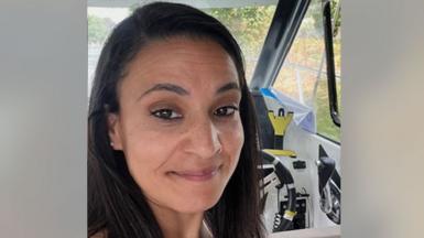 Syreeta Sandhu smiles at the camera. She is in the driver's seat of a car