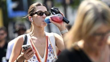 A woman drinks water while carrying a portable fan during hot weather as the UK Health Security Agency (UKHSA) issues an amber extreme heat health alert for East Midlands, West Midlands, East of England, London and South East on August 12, 2025. 