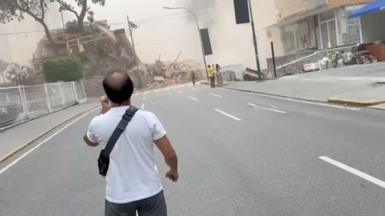 A man stands on a street staring towards a collapsed building.
