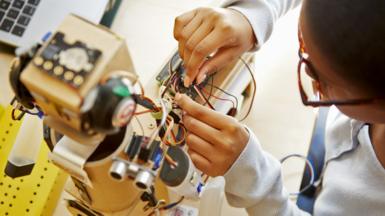 A schoolgirl works on the electronics of a robot as part of a school assignment