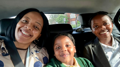 A mum in a car, alongside her two daughters. They are all smiling. 