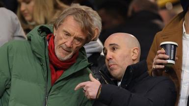 Manchester United chief executive Omar Berrada, wearing a black coat, chats with minority shareholder Sir Jim Ratcliffe in the stands at Old Trafford