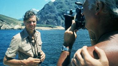 Sir David Attenborough being filmed in front of the sea and mountains for Life on Earth in 1979