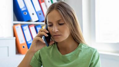 A stock image of a lady in a green t-shirt looking mildly frustrated while on her mobile phone.