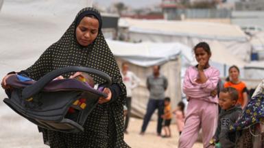 Shaima al-Louh, 24, carries her three-month-old daughter, Jilan Zarrouk, at a makeshift tent camp for displaced Palestinians in al-Mawasi, on the outskirts of Khan Younis in the southern Gaza Strip (9 April 2025)