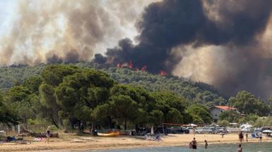 Beachgoers watching nearby smoke and flames billowing from mountain