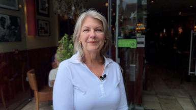 Amanda Brighton, is wearing a white top and is standing outside a restaurant