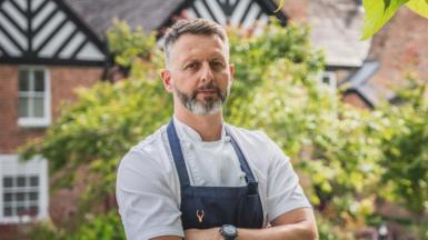 Mark Birchall in his chef whites and dark apron outside Moor Hall, which has a Tudor black and white roof