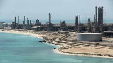 A file photo of Aramco's Ras Tanura oil refinery and oil terminal, which lies along a stretch of coast. The site comprises a network of several tall chimney-shaped structures and smaller buildings. It is daytime and the water along the coastline is a clear blue.