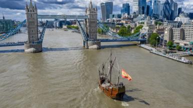 The Nao Santa María flagship sails toward Tower Bridge, which has its bascules raised.