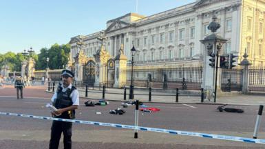 Remnants of an e-scooter crash outside Buckingham Palace with police tape and officers seen in the foreground. 