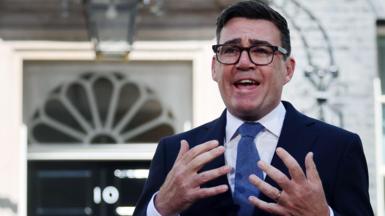 Andy Burnham, dressed in a navy suit, white shirt and ties, stands in front of No 10 Downing Street making a speech