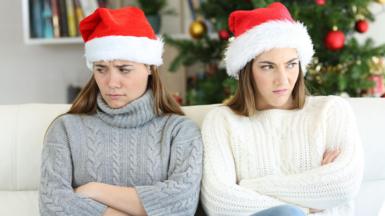 Two sisters with their arms folded, looking cross, at Christmas while wearing father Christmas hats