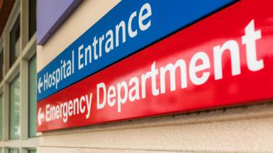 An image of a hospital sign showing the main entrance and the emergency department. The signs are blue and red and have arrows.