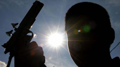 A silhouette of a young man holding a gun