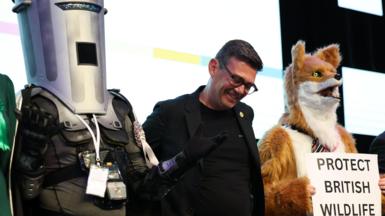 A smiling Andy Burnham stands alongside Count Binface while standing beside a costumed fox after being announced the winner of the Makerfield election.