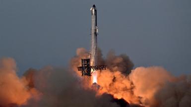 A rocket takes off with smoke and fire coming out the bottom illuminating the bottom orange