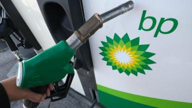 A petrol pump handle being held in front of a BP logo