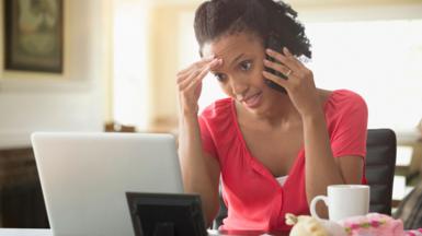 A woman stares at her computer screen while talking on the phone. She looks frustrated