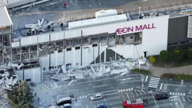 A birds-eye view of Aeon Mall with broken windows and debris in the carpark 