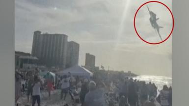 Jet flying above a crowd on a beach with a red circle around it.