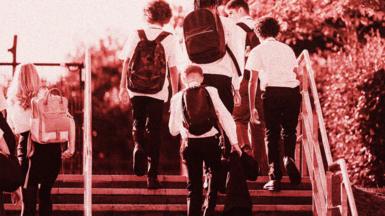Photo of six teenage schoolchildren walking up steps. They are wearing dark trousers and skirts, with white shirts. Some are carrying rucksacks on their backs. 