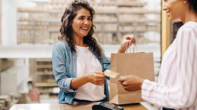 Smiling woman paying with card in shop and holding a brown paper bag