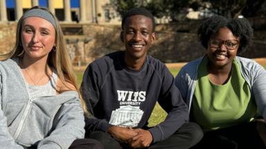 Three students sit on a university lawn 