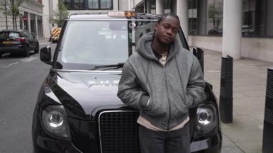 A man wearing a grey hoodie standing in front of a black cab
