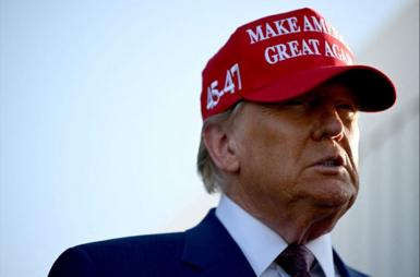 Donald Trump wearing a red MAGA hat with his face partially obscured by shadow