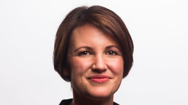 A headshot of a woman smiling at a camera. She has short brown hair. The background is white.