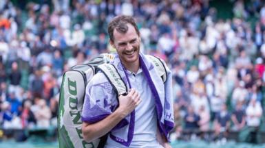 Jamie Murray smiles and is carrying a backpack