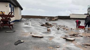 People are seen cleaning up a car park after debris are strewn over the road.