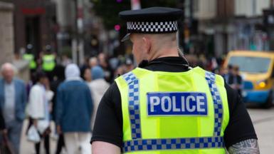The back of the head of a policeman in uniform on patrol in a city, blurred out people are seen in front of him