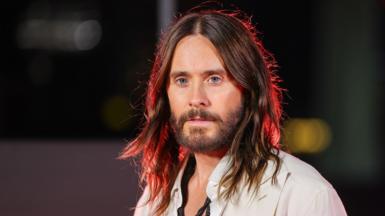 Jared Leto looks toward camera while standing against a dark background at the premiere of Tron: Ares in 2025.