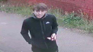 A still image of CCTV footage taken of a man with short brown hair, black jacket 