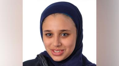 A headshot photo of Sara El-Khawas wearing a hijab and looking at the camera smiling against a white background.