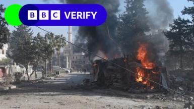 A flaming vehicle on a street in Idlib, Syria. The BBC Verify logo is above it 