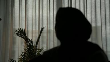Outline of a woman against a window with curtains drawn. 