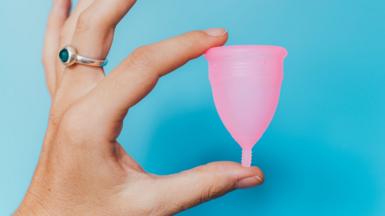 A woman's hand holding a menstrual cup between her thumb and finger