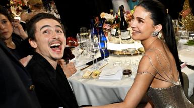 Timothee Chalamet and Kylie Jenner together at the dinner table at the Goilden Globes. He is laughing and she is touching his arm and looking at him