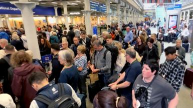 A crowd of people at London St Pancras station in London. They're carrying rucksacks or suitcases as they wait to go through departures and board a Eurostar train across the Channel.