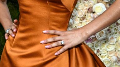 Actress Zendaya poses for the camera with her hands on her hips. She is wearing a burnt orange dress with manicured nails. On the fourth finger of her left hand is a large diamond ring, suggesting she has got engaged.