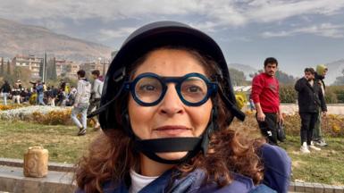 Lina Sinjab, a Syrian BBC journalist with brown hair and with thick-rimmed dark blue circular glasses, wearing a press helmet, having returned to Damascus after the fall of the Assad regime in 2024