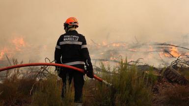 A firefighter holds a hose as he looks at burning vegetation