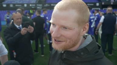 Ed Sheeran looks to the BBC reporter. He is smiling and has cropped ginger hair