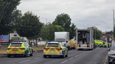 A number of police vehicles close off dual carriageway in Merseyside. The road has trees lined down the middle