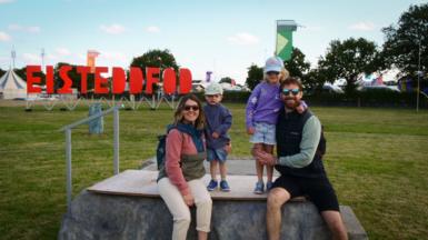 Sioned a Dylan gyda'u plant Nedw a Greta ar y Maen Llog. Roedd Nedw a Greta yn edrych ymlaen at ffeindio stondin i liwio ar ôl i Mam a Dad gael gweld Band Deiniolen yn cystadlu yn y pafiliwn
